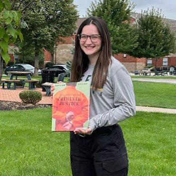 Elizabeth standing next to a tree holding a Criminal Justice book